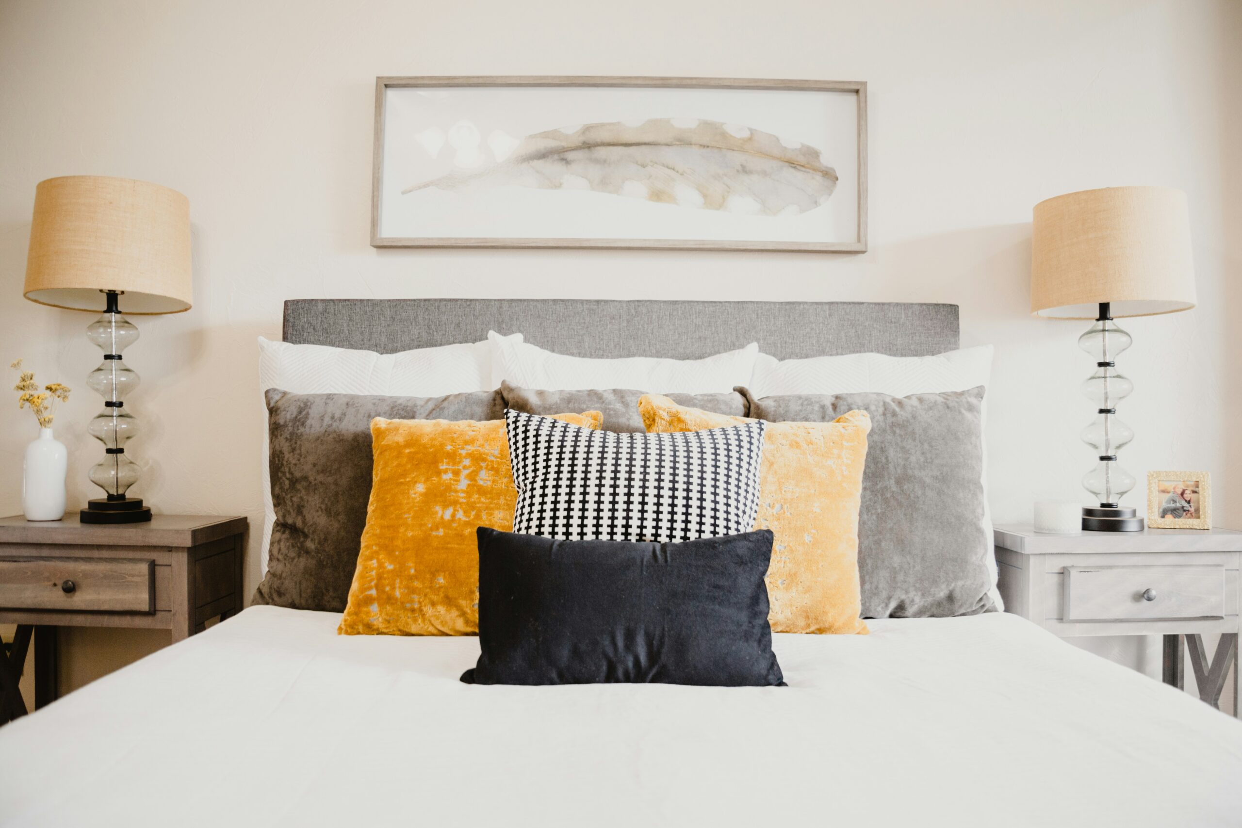 Bedroom interior with a neatly made bed, layered pillows in yellow, black, and gray, and matching lamps on nightstands.