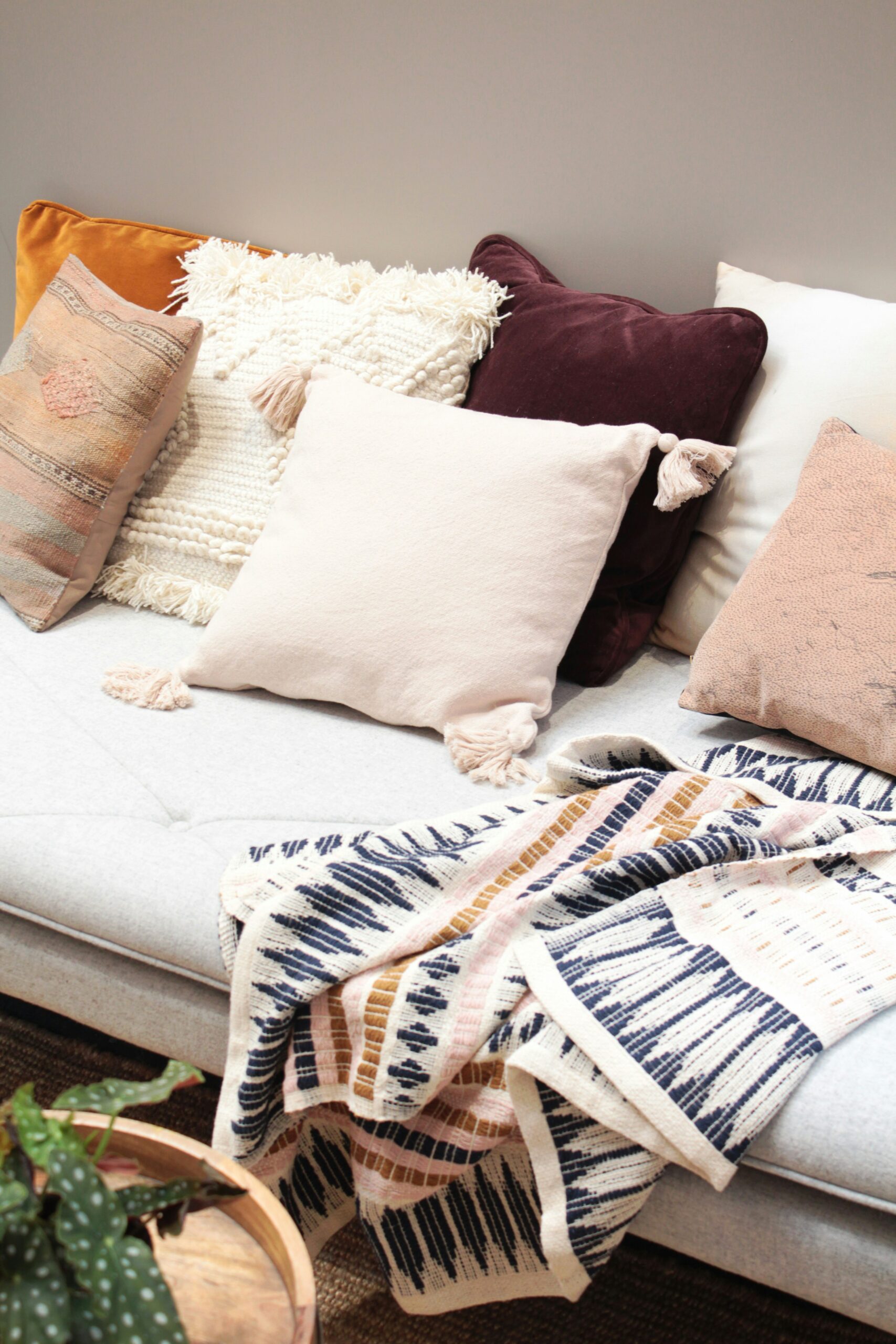 Cozy sofa with assorted decorative pillows in neutral and earthy tones, with a patterned throw blanket.